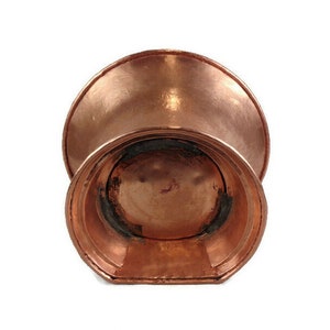 May include: A copper planter with a wide, flared top and a rounded bottom. The planter has a smooth, polished finish.
