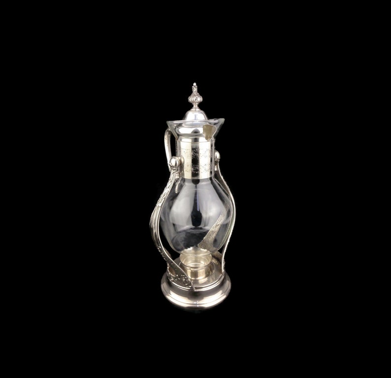 May include: Silver and glass beverage dispenser with a decorative handle and a base with a candle holder.