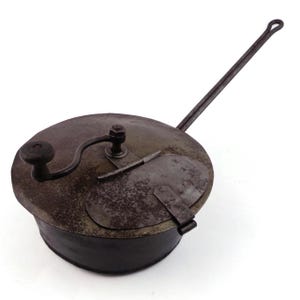May include: Antique metal popcorn popper with a long handle and a crank. The popper has a round, lidded design with a small door and a wooden knob. The metal has a rustic, aged appearance.