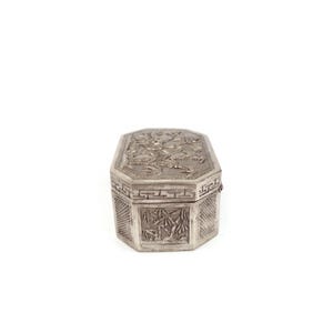 May include: A silver octagonal box with intricate floral and geometric designs. The box is closed and has a hinged lid.