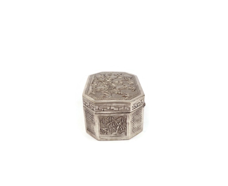 May include: A silver octagonal box with intricate floral and geometric designs. The box is closed and has a hinged lid.