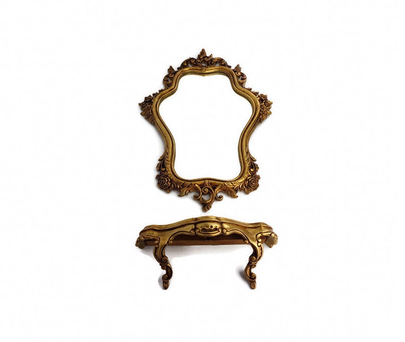 May include: A gold-colored ornate mirror with a decorative frame and a matching gold-colored vanity table with a shelf.