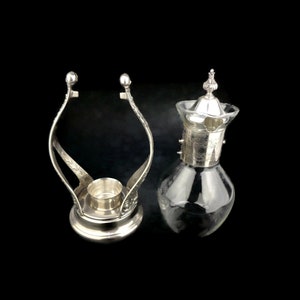 May include: Silver plated candle holder with a glass carafe with a silver lid. The candle holder has a decorative design and the carafe has a floral design.