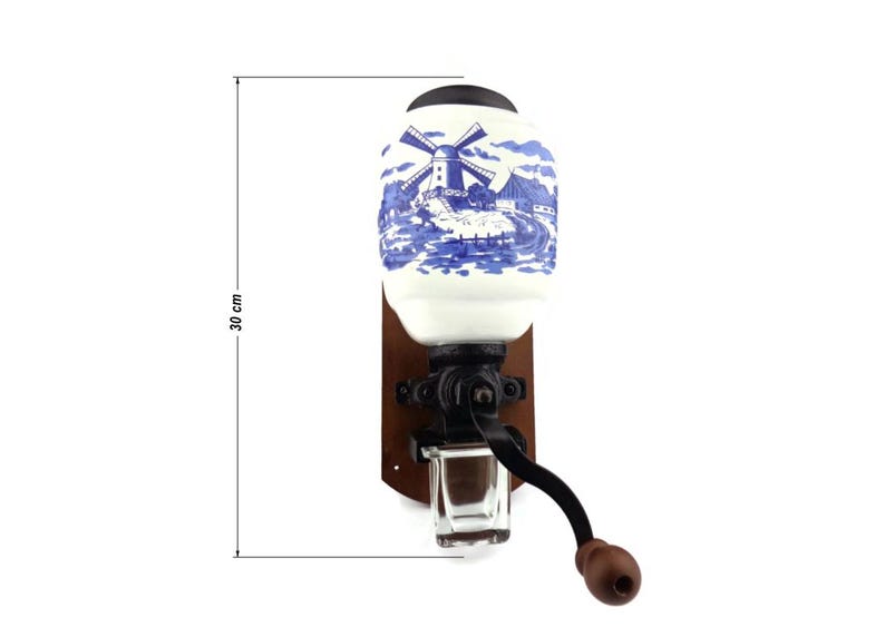 May include: A vintage, wall-mounted coffee grinder with a white ceramic jar featuring a blue and white windmill scene. The grinder has a wooden base and a black metal crank handle. The jar is 30 cm tall.