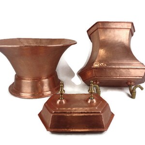 May include: Three copper planters with decorative spouts. The planters are in different shapes and sizes. The largest planter is a wide bowl shape with a flared rim. The middle planter is a tall, hexagonal shape with a flared rim. The smallest planter is a rectangular shape with a decorative lid.