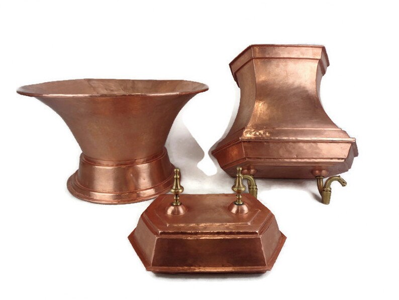 May include: Three copper planters with decorative spouts. The planters are in different shapes and sizes. The largest planter is a wide bowl shape with a flared rim. The middle planter is a tall, hexagonal shape with a flared rim. The smallest planter is a rectangular shape with a decorative lid.