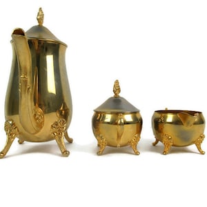 Può includere: Un set da tè dorato con teiera, lattiera e zuccheriera. Ogni pezzo presenta un design floreale decorativo e poggia su tre piedini decorati.
