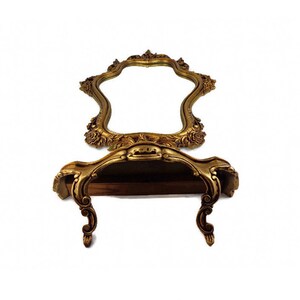 May include: A gold-toned ornate mirror with a shelf underneath. The mirror has a scalloped edge and intricate floral details. The shelf is also decorated with ornate details.