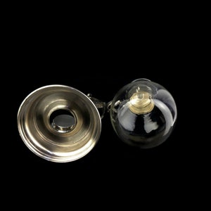 May include: A silver and glass bottle stopper with a round, clear glass top and a silver base. The glass top has a small, round, silver cap inside.