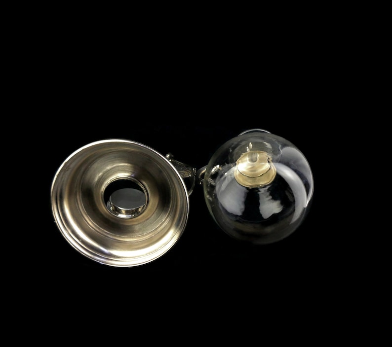 May include: A silver and glass bottle stopper with a round, clear glass top and a silver base. The glass top has a small, round, silver cap inside.