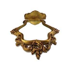 May include: A gold-toned ornate mirror with a decorative frame. The frame has a scalloped edge and intricate floral designs.