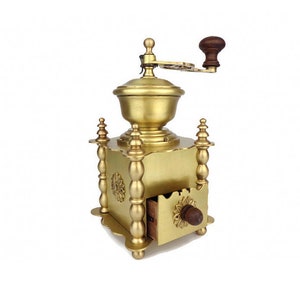 May include: A vintage brass coffee grinder with a wooden handle and drawer. The grinder has a decorative design with ornate details.