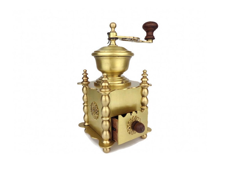May include: A vintage brass coffee grinder with a wooden handle and drawer. The grinder has a decorative design with ornate details.