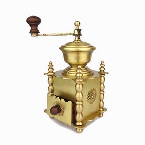 May include: A gold-toned manual coffee grinder with a wooden handle and a drawer for collecting the ground coffee beans.
