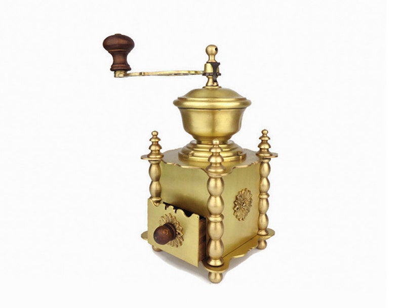 May include: A gold-toned manual coffee grinder with a wooden handle and a drawer for collecting the ground coffee beans.