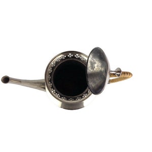 Puede incluir: Una tetera de plata con un asa de mimbre y una tapa extra&iacute;ble. La tetera tiene un dise&ntilde;o decorativo alrededor del borde.