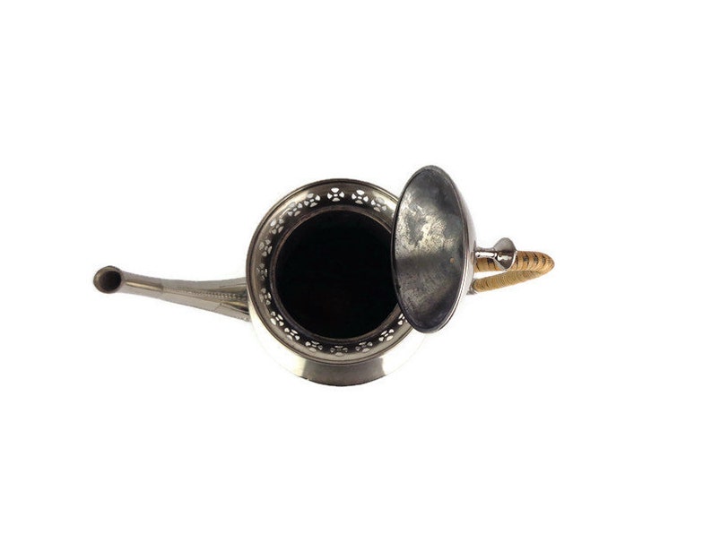 Puede incluir: Una tetera de plata con un asa de mimbre y una tapa extra&iacute;ble. La tetera tiene un dise&ntilde;o decorativo alrededor del borde.