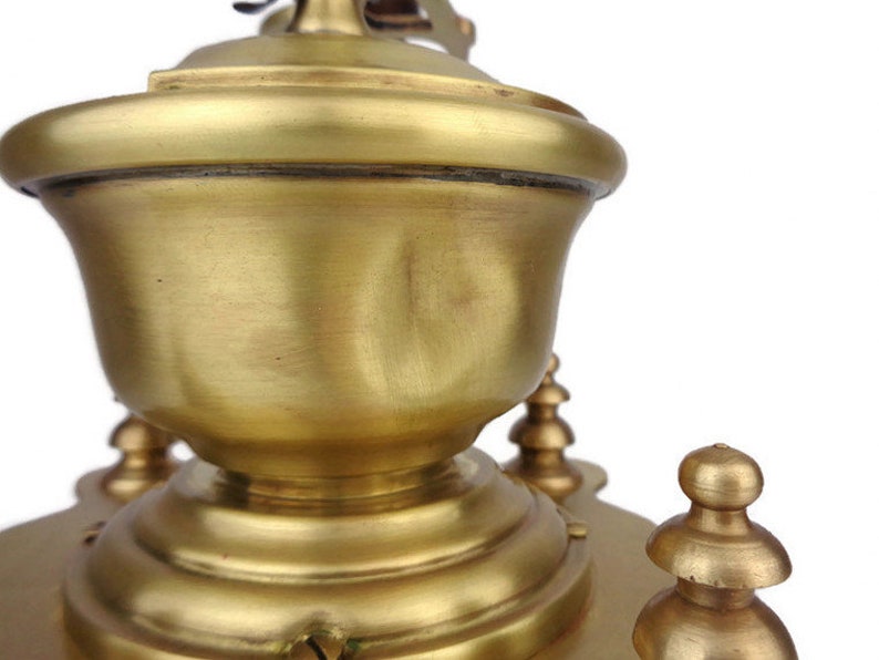 May include: A vintage brass coffee grinder with a round, ornate top and a decorative base. The grinder has a smooth, polished finish and intricate details.