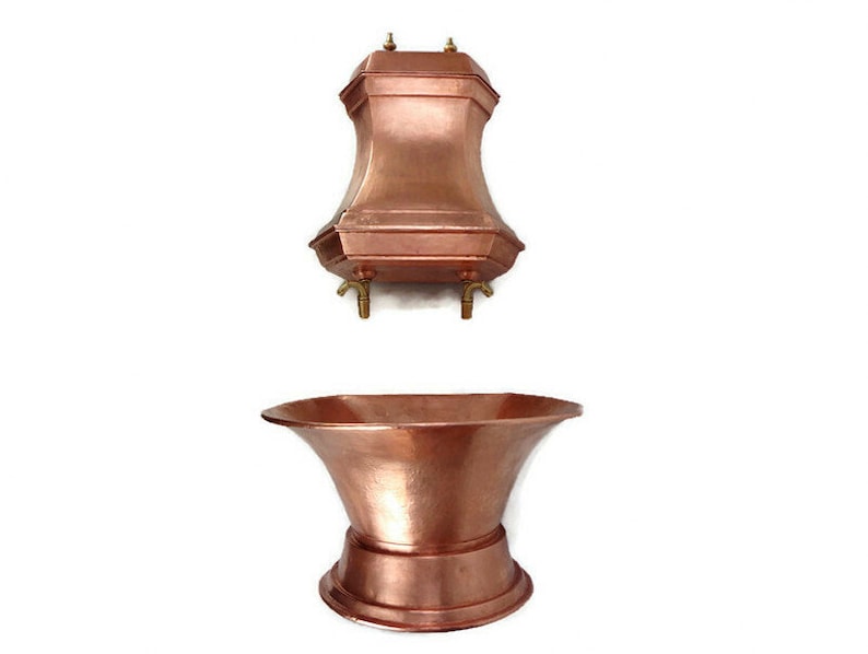 May include: A copper bathtub with a copper faucet and spout. The bathtub is freestanding and has a rounded shape. The faucet is attached to a wall-mounted copper fixture.