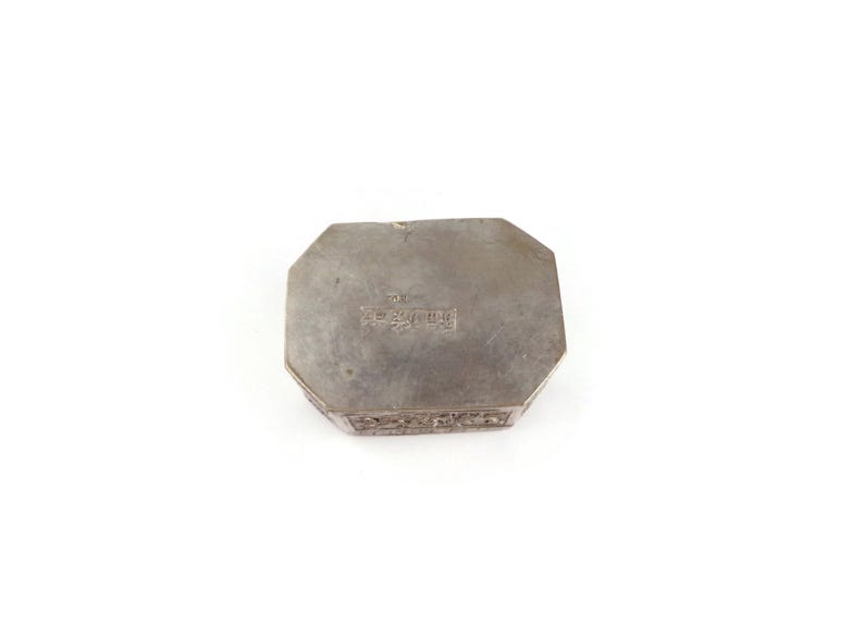 May include: Octagonal silver box with intricate engraved details on the sides and a stamped inscription on the bottom.