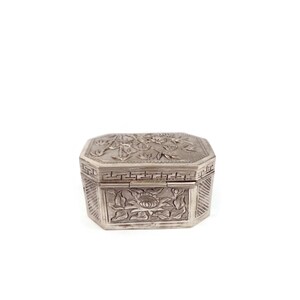 May include: A silver box with an intricate floral design. The box has a hinged lid and is decorated with a repeating pattern of flowers and leaves.