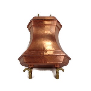 May include: A copper water dispenser with a hexagonal top and three brass spouts. The dispenser has a hammered finish and sits on three brass legs.