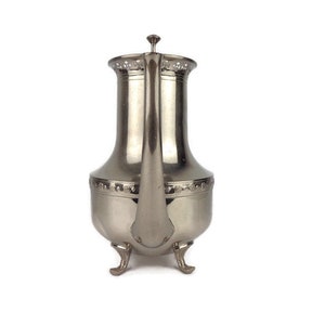 Puede incluir: Una tetera de plata con un dise&ntilde;o decorativo y tres patas. La tetera tiene un pico y una tapa.