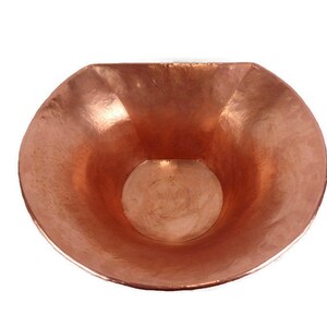May include: A copper bowl with a hammered finish. The bowl is half-round and has a wide, shallow opening.
