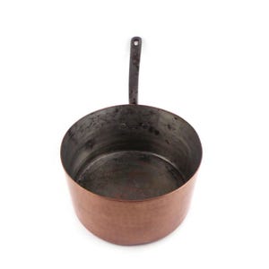 May include: A copper-colored saucepan with a long, dark handle. The interior of the pan is dark, showing signs of use. The handle has a hole at the end for hanging. The pan is round and has a slightly flared rim. Kitchenware.