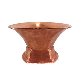 May include: A copper planter with a wide, flared top and a hexagonal base. The planter has a hammered finish and a warm, reddish-brown color.
