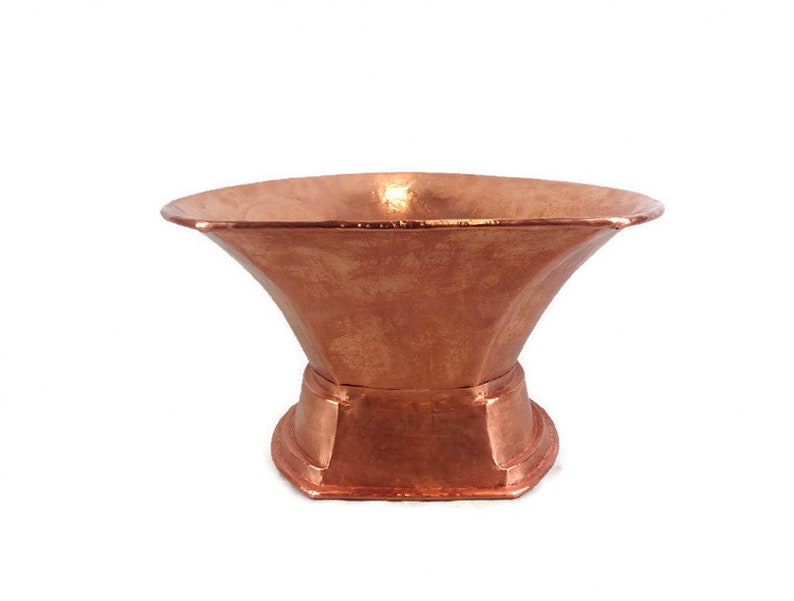 May include: A copper planter with a wide, flared top and a hexagonal base. The planter has a hammered finish and a warm, reddish-brown color.