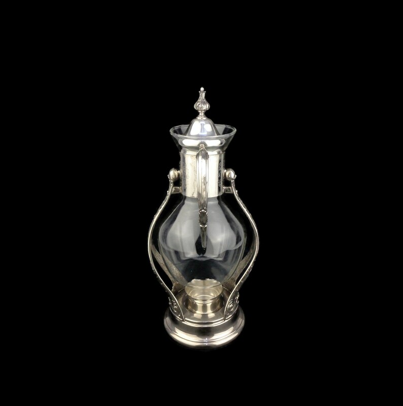May include: A silver and glass coffee pot with a decorative design. The pot has a clear glass body and a silver lid with a finial.