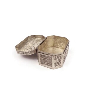 May include: A silver, octagonal trinket box with intricate floral and geometric designs. The box is open, revealing the empty interior.