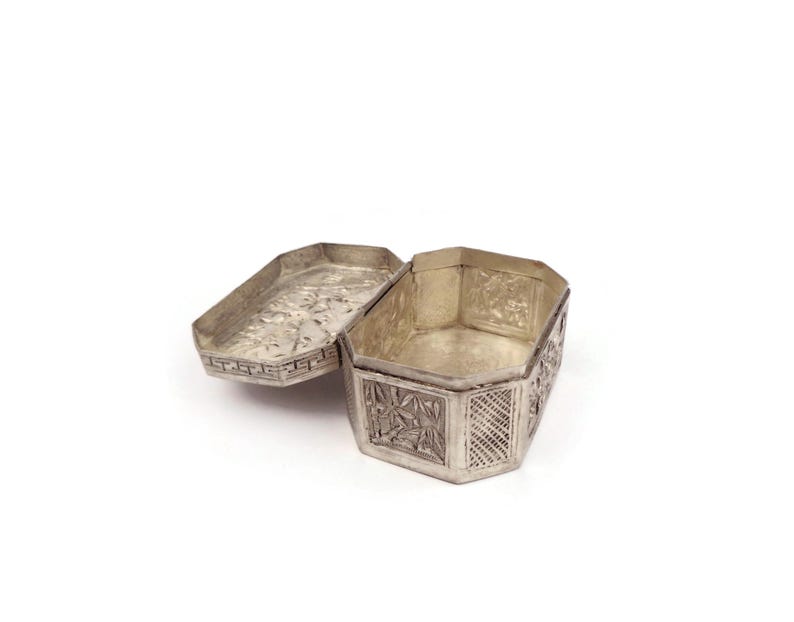 May include: A silver, octagonal trinket box with intricate floral and geometric designs. The box is open, revealing the empty interior.