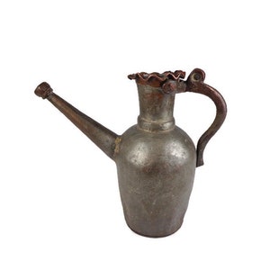 Peut inclure: Un arrosoir antique en argent avec un bec et une poignée en cuivre. La poignée est décorée d'un motif.