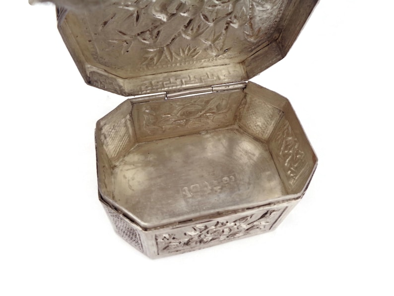 May include: A silver octagonal box with an intricate floral design on the lid and base. The box is open, revealing a plain interior.