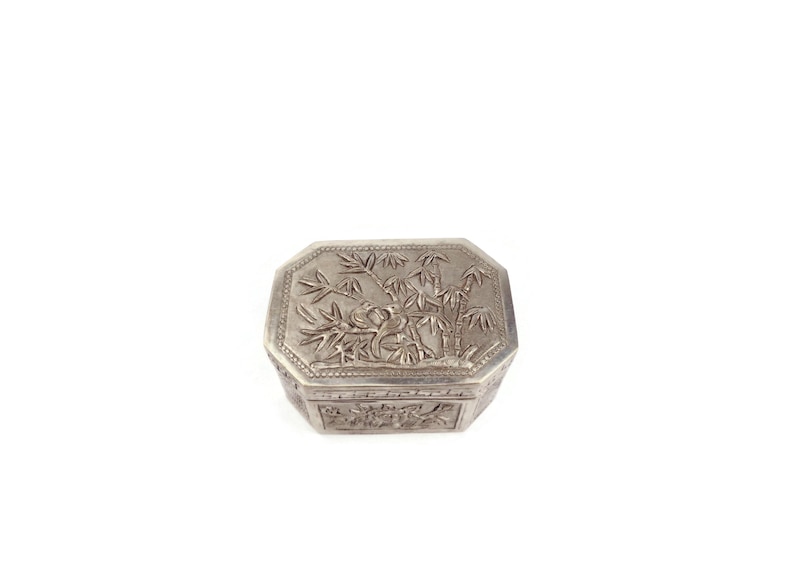 May include: A silver trinket box with an intricate design of bamboo plants and birds. The box is octagonal in shape and has a hinged lid.