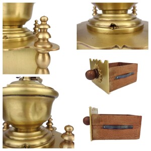 May include: Antique brass coffee grinder with a wooden drawer. The grinder has a decorative top with a finial and a wooden handle. The drawer is made of wood and has a brass pull.