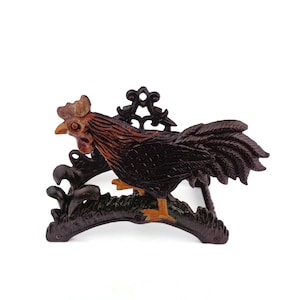 Könnte beinhalten: Dekorative Gusseisen-Hahn-Figur. Der Hahn ist braun mit orangefarbenen und gelben Akzenten und sitzt auf einem dekorativen Sockel. Die Figur hat ein detailliertes Design und eignet sich für die Inneneinrichtung.