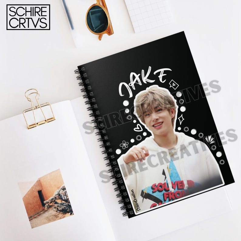 May include: Black spiral notebook with a white border and the name "JAKE" written in white. A photo of a young man with brown hair is on the cover. The photo is surrounded by white doodles.