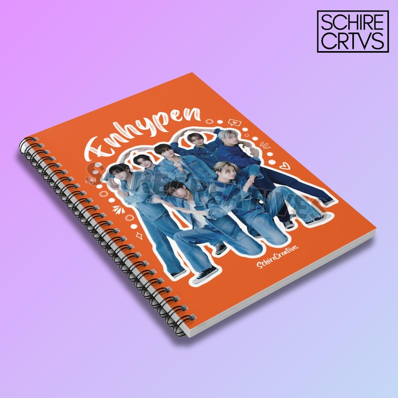 May include: Orange spiral notebook with a white graphic of a K-pop boy band, Enhypen, in a circle with white doodles around the band. The text "Enhypen" is written in white cursive on the cover.