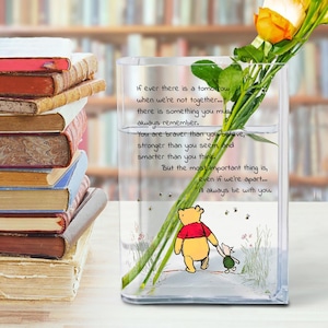 May include: A clear glass vase with a Winnie the Pooh illustration and text. The vase holds flowers and is next to a stack of books. The text reads: "If ever there is a tomorrow... I'll always be with you."