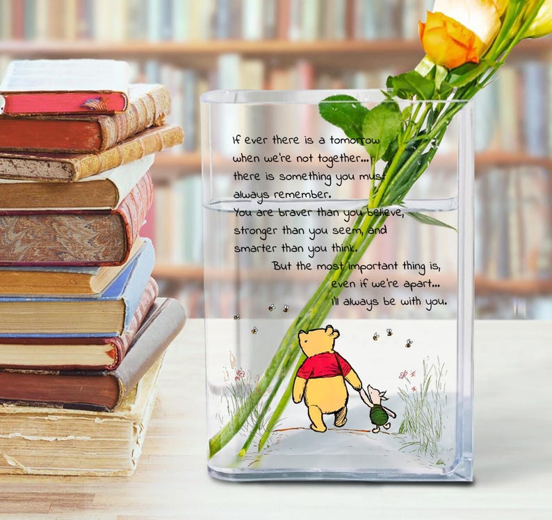 May include: A clear glass vase with a Winnie the Pooh illustration and text. The vase holds flowers and is next to a stack of books. The text reads: "If ever there is a tomorrow... I'll always be with you."
