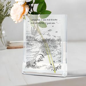 Puede incluir: Jarr&oacute;n rectangular de cristal transparente con una ilustraci&oacute;n en blanco y negro de un paisaje y una cita. El jarr&oacute;n contiene un tallo de flor con una flor de color melocot&oacute;n. La cita dice: "Sometimes, I sits and thinks and sometimes, I just sits..."