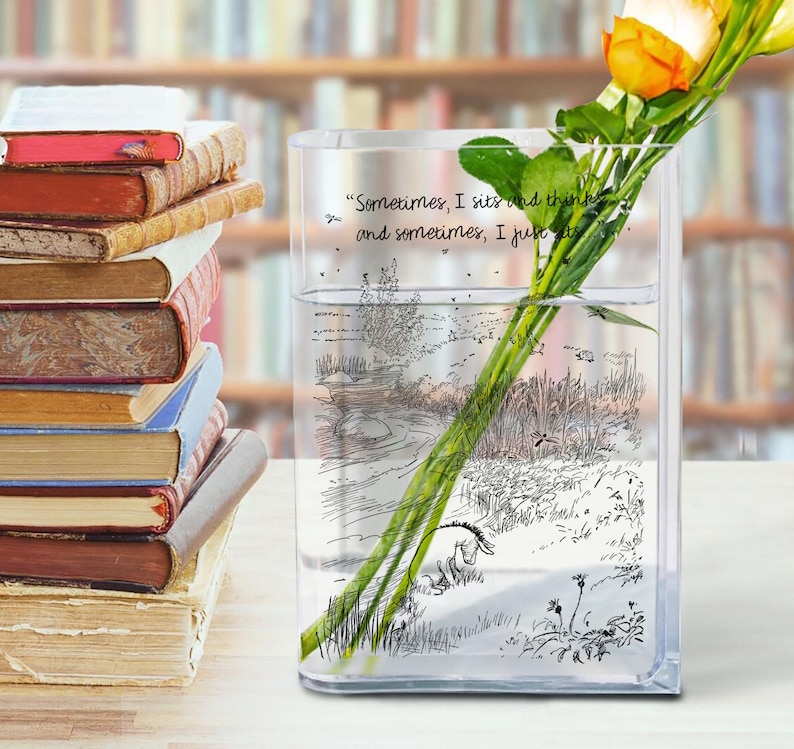 Puede incluir: Un jarr&oacute;n de vidrio transparente y rectangular con una ilustraci&oacute;n y cita de Winnie the Pooh, que contiene rosas amarillas y naranjas. Una pila de libros antiguos est&aacute; a la izquierda. El jarr&oacute;n est&aacute; lleno de agua.