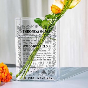 May include: Clear glass vase with the text "THRONE OF GLASS" and other phrases. The vase has a rectangular shape and contains water and yellow roses. The text includes a deer and castle illustration.