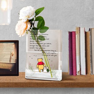May include: A clear rectangular vase with a Winnie the Pooh illustration and text. The vase holds white and peach-colored flowers. The text reads, "If ever there is a tomorrow... I'll always be with you."