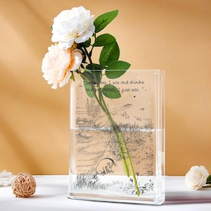 Puede incluir: Un jarr&oacute;n rectangular de vidrio transparente con una ilustraci&oacute;n de Winnie the Pooh y la cita "Sometimes, I sits and thinks and sometimes, I just sits." El jarr&oacute;n contiene agua y un tallo de rosas blancas y melocot&oacute;n.