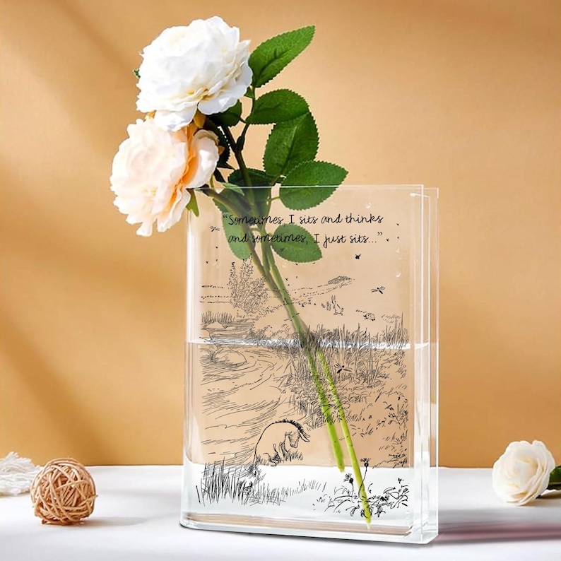 Puede incluir: Un jarr&oacute;n rectangular de vidrio transparente con una ilustraci&oacute;n de Winnie the Pooh y la cita "Sometimes, I sits and thinks and sometimes, I just sits." El jarr&oacute;n contiene agua y un tallo de rosas blancas y melocot&oacute;n.