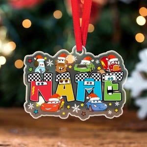 Può includere: Un ornamento natalizio personalizzato con il nome "NAME" in lettere colorate, ognuna ornata da un cappello di Babbo Natale. L'ornamento presenta auto dei cartoni animati e accenti festivi di fiocchi di neve e stelle, sospeso da un nastro rosso.
